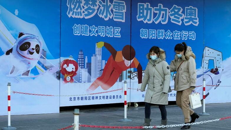 Zwei Frauen gehen an Werbetafeln vorbei, die für die bevorstehenden Olympischen Winterspiele in Peking werben.