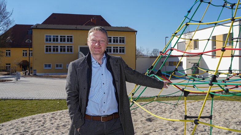 Sohlands Bürgermeister Hagen Israel steht auf dem neu gestalteten Außengelände der Grundschule am Frühlingsberg. Hinter ihm sind der sanierte Schul-Altbau (l.) und der Hort-Neubau (r.) zu sehen.
