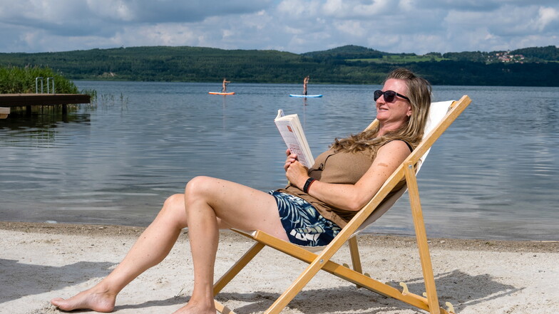 Am Strand des Hotels "Insel der Sinne" am Berzdorfer See findet diese Frau Ruhe und Entspannung. Stand-up-Paddler auf dem See genießen ebenfalls die Atmosphäre.