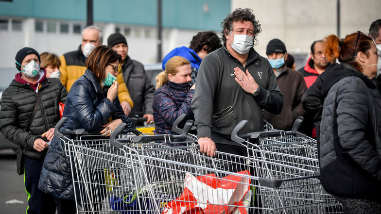 Italien, Casalpusterlengo: Menschen tragen Atemschutzmasken und stehen vor einem Supermarkt in einer Schlange. Nach dem Tod zweier Menschen sind Teile des öffentlichen Lebens zum Erliegen gekommen.