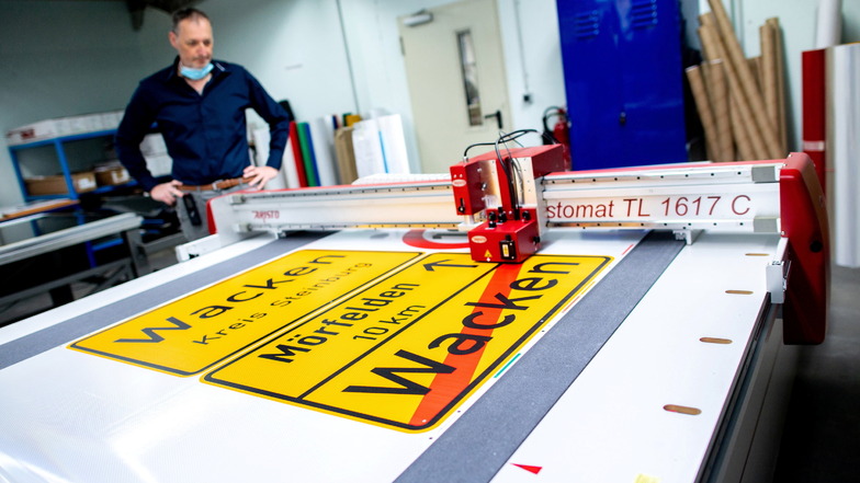 Michael Mazur, Abteilungsleiter Druckverfahren in der Fritz Lange GmbH, begutachtet den automatischen Zuschnitt einer Ortstafel von Wacken auf spezieller selbstklebender Folie.