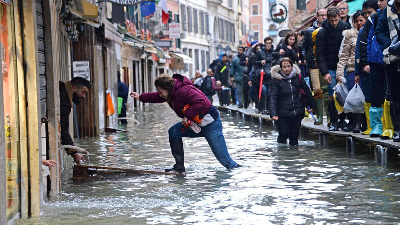 Eine Frau versucht, eine überflutete Straße zu überqueren. Nach dem schweren Hochwasser in Venedig ist die Lage weiterhin angespannt.