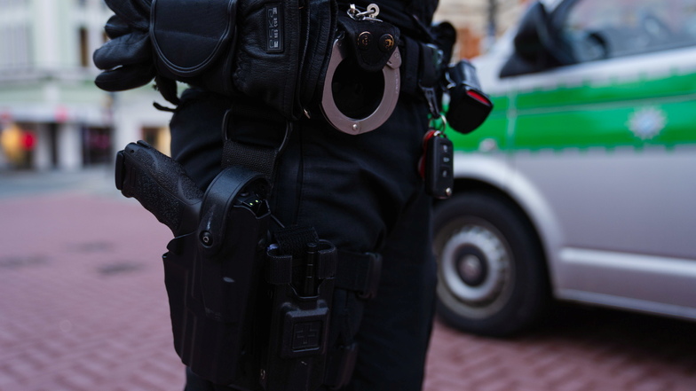 Ein Polizeibeamter steht in der Fußgängerzone von Hof neben seinem Einsatzfahrzeug.