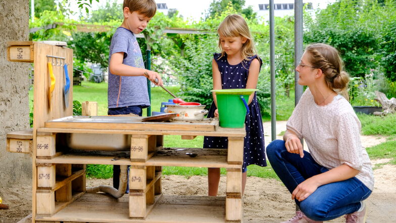 Emil und Evelina backen in der Matschküche der Kita „Kinderkreis Natur, Heimat und Gesundheit“ einen Sandkuchen. Debora Centner schaut ihnen dabei zu. Die Sprachfachkraft möchte mit Kindern und Eltern zusammen weitere neue Spielbereiche schaffen.