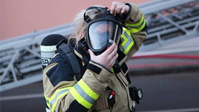 Eine Frau der Feuerwehr legt ihre Atemschutzmaske an.