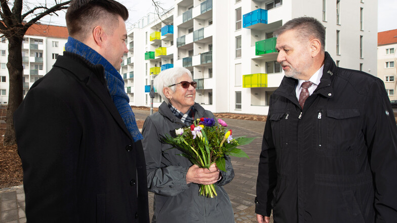 Mit einem Sträußchen Blumen begrüßen die Vorstände Torsten Munk (l.) und Mathias Schulze die neue Mieterin Monika Guhr vor dem Neubau an der Struvestraße.