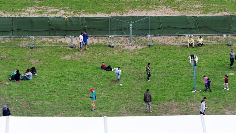 Blick von oben ins Flüchtlingszelt in der Südvorstadt: Kinder spielen Fußball, Menschen sitzen auf dem Boden oder laufen hinter einem mit grünen Planen abgehangenen Zaun umher.