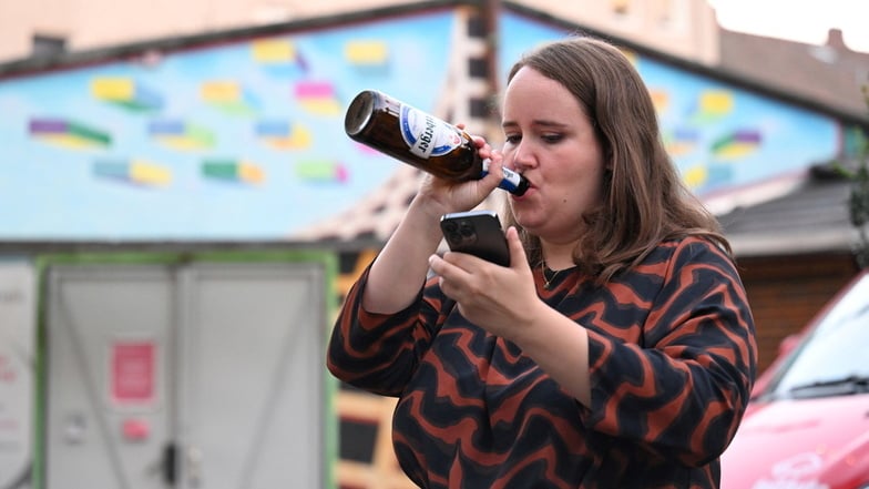 Die Bundesvorsitzende Ricarda Lang trinkt ein Bier, während sie aufs Handy lugt