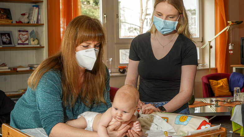 Hebamme Mandy Preusche (l.) untersucht die drei Monate alte Ella. Wegen der Maske würden manche Babys irritiert schauen. Ellas Mama, Eunike Glöß, kann diesen Eindruck bei ihrer Tochter bestätigen.