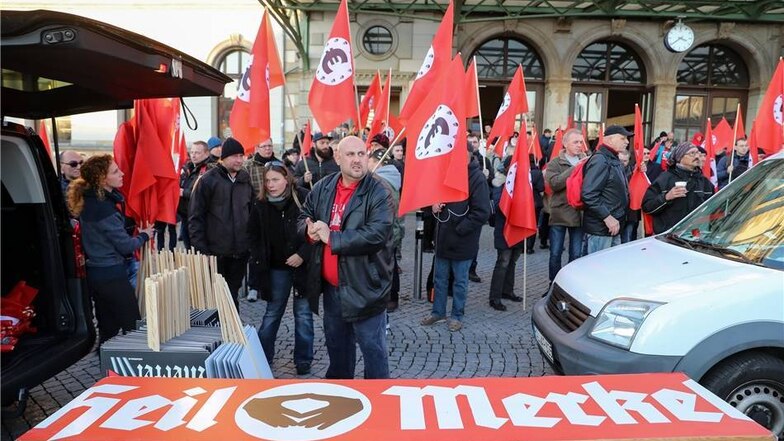 Teilnehmer einer von der "Merkeljugend" angemeldeten rechten Kundgebung auf dem Vorplatz des Hauptbahnhofs. Es sind Fahnen zu sehen, die an die Flaggen der NS-Zeit erinnern - mit einem schwarzen Euro-Symbol in einem weißen Kreis auf rotem Grund.
