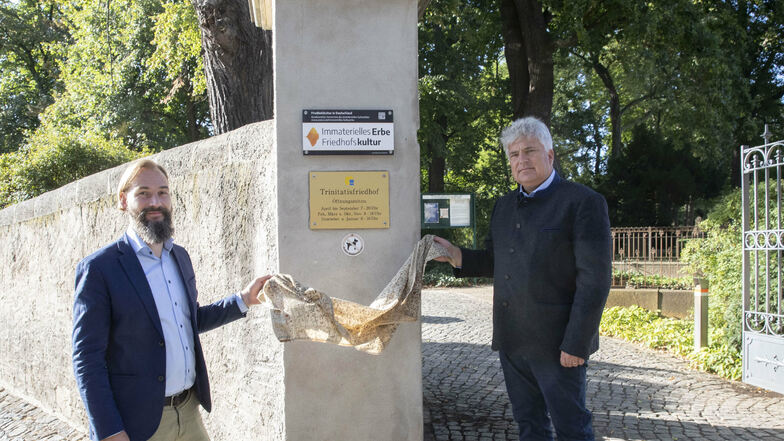 Pfarrer Martin Scheiter und Friedhofsverwalter Andreas Wolf enthüllen die Plakette am Eingang zum Trinitatisfriedhof.