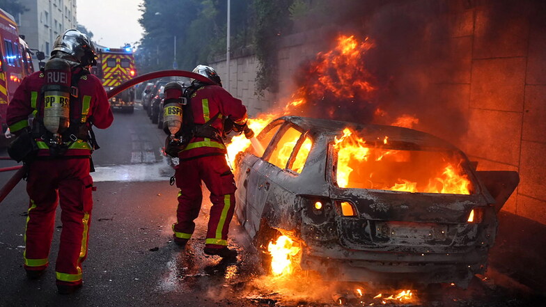 Feuerwehrleute löschen ein brennendes Auto am Rande von Ausschreitungen in Nanterre.