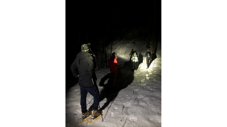 Skilehrer Lukas leuchtet den Teilnehmern am nächtlichen Schneeschuhwandern den Weg.