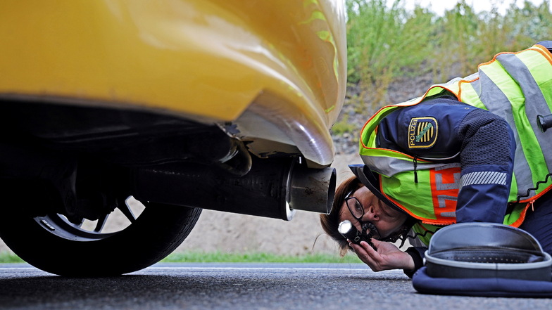 Eine Polizistin kontrolliert den Auspuff eines getunten Hondas.
