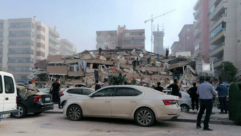 Menschen stehen nach dem Erdbeben in Izmir vor einem zusammengestürzten Gebäude.