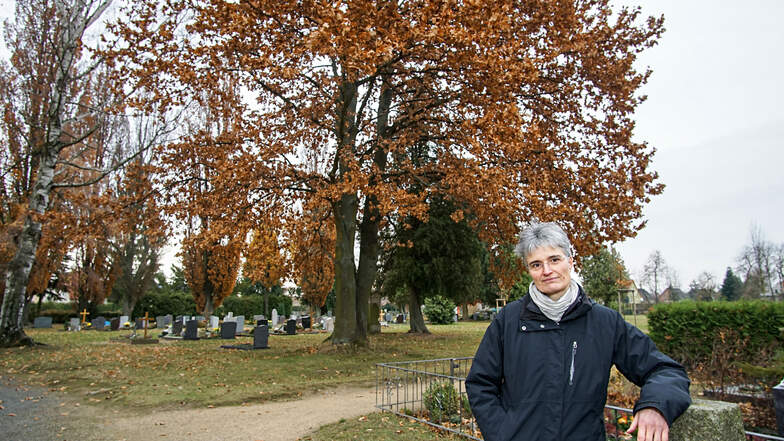 Pfarrerin Susanne Aechtner steht hier am Rand einer Urnen-Gemeinschaftsanlage auf dem Friedhof in Neschwitz. Rund um die große Eiche hinter ihr soll demnächst Platz für Baumbestattungen geschaffen werden.