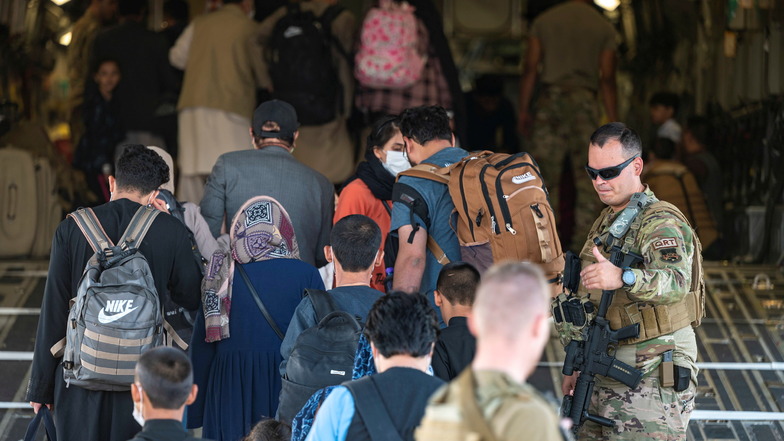 Ein US-Luftwaffenangehöriger (r)sorgt für Sicherheit, als afghanische Flüchtlinge während der Evakuierung vom Hamid Karzai International Airport im Rahmen der Operation Allies Refuge an Bord eines Militärtransportflugzeugs von Typ Boeing C-17 Globemaster 