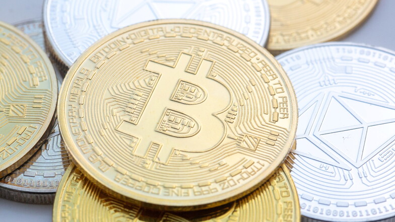 Bitcoins (M) und Ethereum-Münzen sind auf einem Tisch angeordnet.