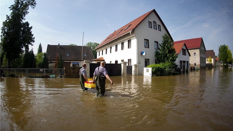 Bürger in Pirna-Copitz tragen am Samstag eine Kiste durch das langsam sinkende Hochwasser der Elbe über eine überflutete Straße.