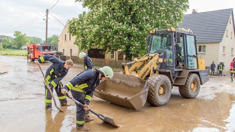 Einsatzkräfte der Feuerwehr beseitigen am Freitag nach heftigen Regenfällen in Oberbobritzsch bei Freiberg Wasser und Schlamm von einer Straße.