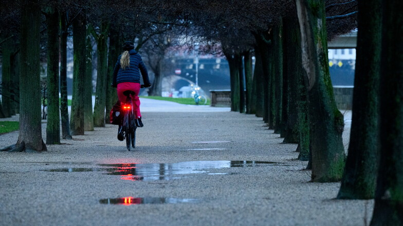 Eine Radfahrerin fährt im Garten des Japanischen Palais in Dresden an Pfützen vorbei: Am Sonntag wird es in Sachsen verbreitet regnerisch.