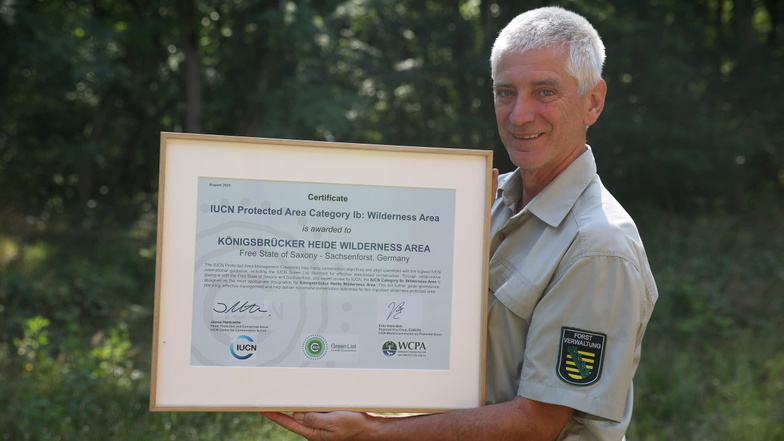 Kaj Krumbiegel von Sachsenforst, verantwortlich für das Gebiet der Königsbrücker Heide, zeigt stolz die Urkunde zur Zertifizierung als Wildnisgebiet.