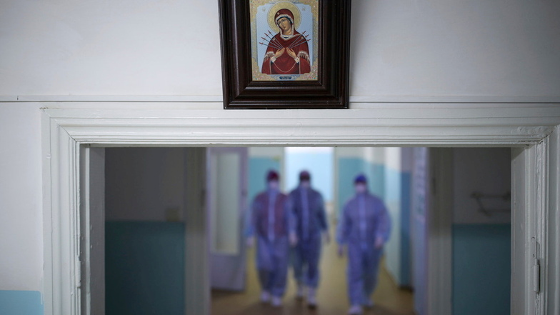 Russland, Poltawskaja: Ein religiöses Bild hängt eingerahmt an der Wand während Sanitäter in Schutzkleidung in einer Intensivstation eines Krankenhauses den Flur entlang gehen.