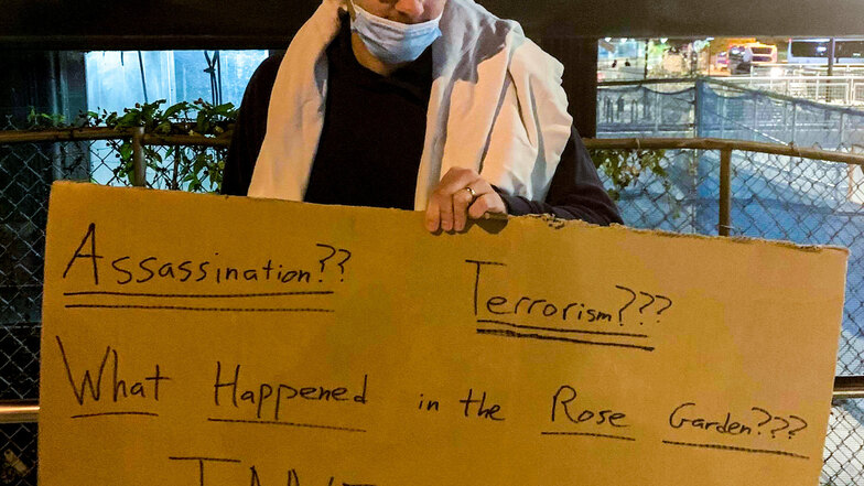 Trump-Anhänger Will steht mit einem Schild mit der Aufschrift "Attentat?? Terrorismus??? Was passierte im Rosengarten??? Ermittelt!!!" vor der Klinik.