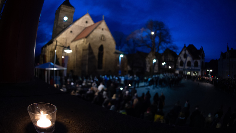 Besucher stehen beim ökumenischen Gottesdienst an der Kirche St. Marien, während eine Kerze auf der Rathaustreppe brennt. 