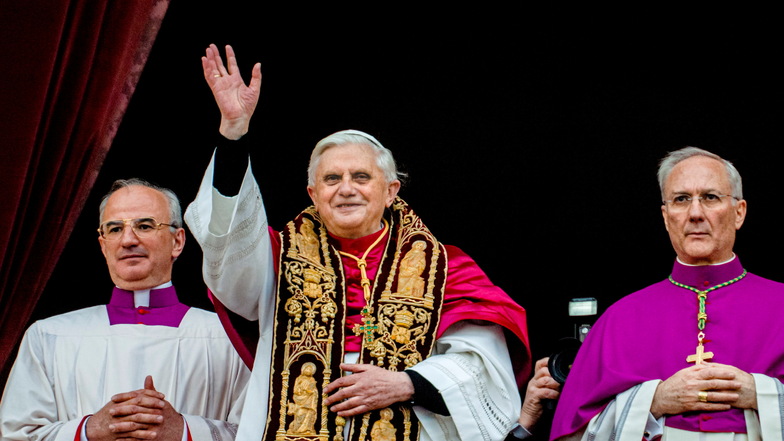 19.04.2005: Papst Benedikt XVI., flankiert von Monsignore Francesco Camaldo (l) und Bischof Piero Marini, grüßt die Menge vom zentralen Balkon des Petersdoms im Vatikan kurz nach seiner Wahl.