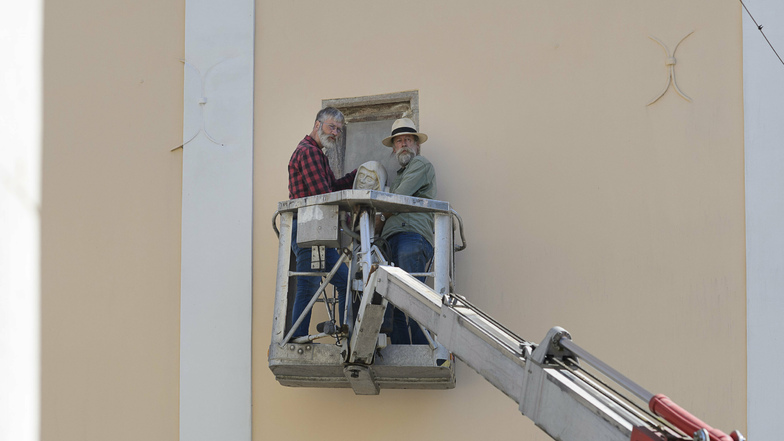 Hans (links) und Michael Herbig von der Firma Herbig Denkmalpflege aus Ostritz bringen den aus Sandstein gefertigten Mönchskopf in der Fensternische an.