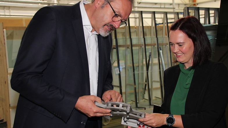 Prokuristin Christiane Düffort und Staatssekretär Stefan Brangs betrachten eines der Scharniere, die vom Innovationsassistenten gemeinsam mit weiteren Mitarbeitern der Vitrinen- und Glasbau Reier GmbH entwickelt wurde.