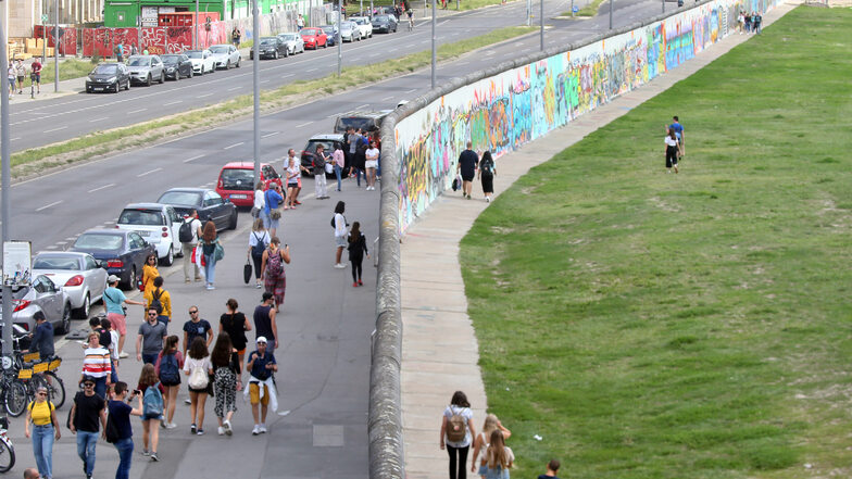 Menschen gehen auf beiden Seiten des längsten, noch erhaltenen Teilstücks der Berliner Mauer, der East Side Gallery.