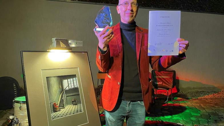 Frank Kunert mit dem Preis, der Urkunde und seiner Siegerarbeit „Hoch hinaus“ nach der Verleihung des Heinrich-Zille-Karikaturenpreises 2021 im Hof des Radeburger Heimatmuseums.