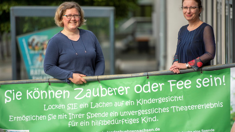Die Vorsitzende und stellvertretende Vorsitzende vom Freundeskreis der Landesbühnen Sachsen, Caroline Mirisch (l.) und Barbara Weidlich stehen mit einem Banner des Freundeskreises vor dem Theater.