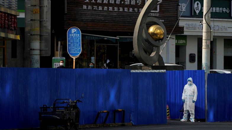 Ein Arbeiter in Schutzkleidung steht in Peking an Metallbarrieren, die im Rahmen der COVID-19-Kontrollen um verschlossene Geschäftshäuser errichtet wurden.