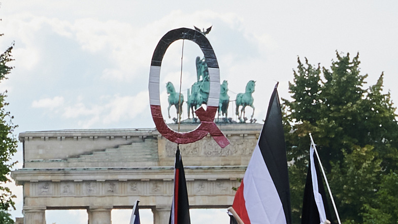Reichsflaggen und ein Q in den selben Farben halten Demonstranten vor dem Brandenburger Tor. Q steht für QAnon.