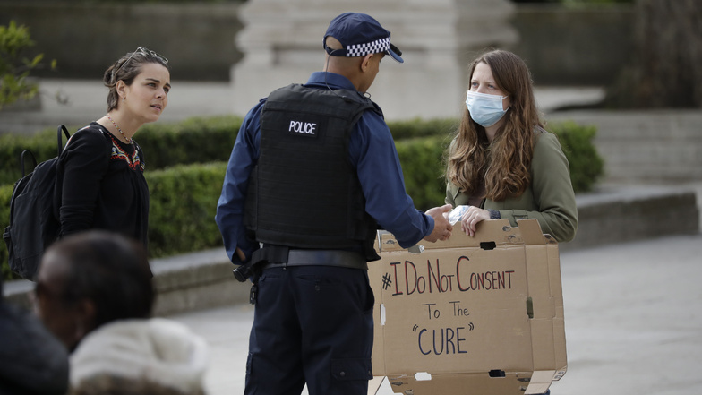 Ein Polizeibeamter spricht in London mit Demonstranten, die sich mit Schildern mit der Aufschrift "Ich stimme der "Kur" nicht zu" versammelt haben, um gegen die Restriktionsmaßnahmen der Regierung zu protestieren.
