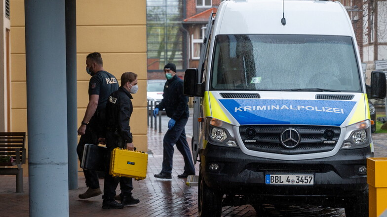 Ein Mitarbeiter der Kriminalpolizei geht mit zwei kleinen Handkoffern auf dem Gelände einer Potsdamer Behinderten-Wohnanlage zu einem Polizeiauto.