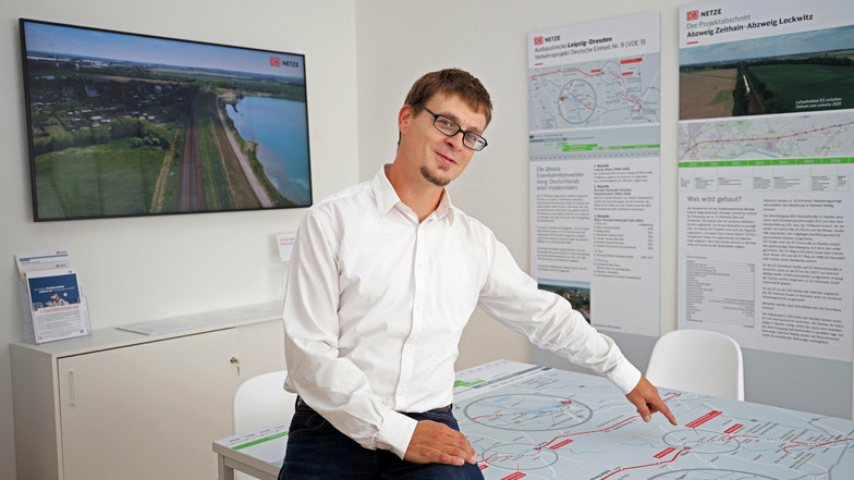 Holger Braune von der DB Netz AG zeigt auf den Tisch im neuen Nünchritzer Info-Punkt, auf dem Landkarten geklebt sind. Im Hintergrund ist ein Bildschirm zu sehen.