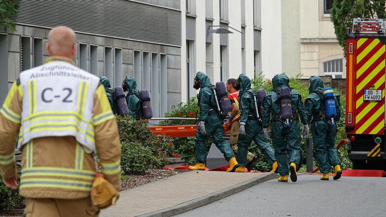 Mehrere Feuerwehrleute mit Schutzanzügen bringen einen der am Freitag in Riesa verunglückten Mitarbeiter einer Reinigungsfirma ins Klinikum Dresden-Friedrichstadt.