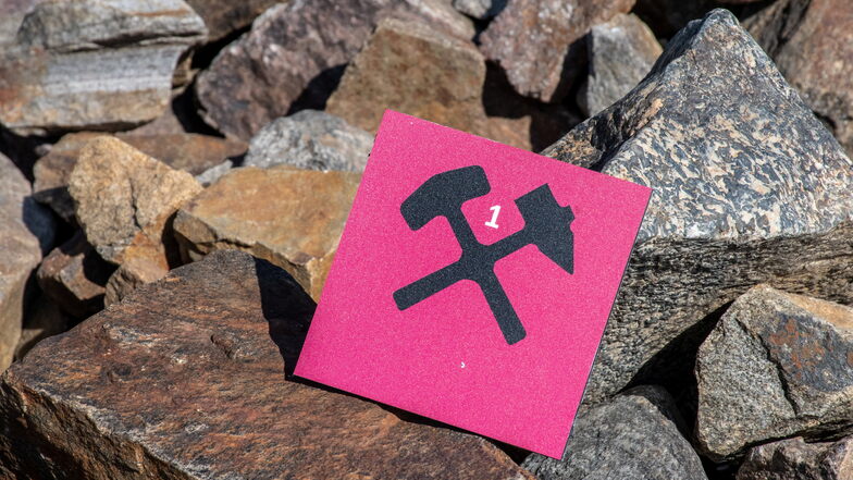 Schlägel und Bergeisen - beide Werkzeuge gekreuzt, stellen das traditionelle Symbol für den Bergbau dar. Am Lehrpfad finden sie Wanderer von knalligem Pink und Türkis umgeben.