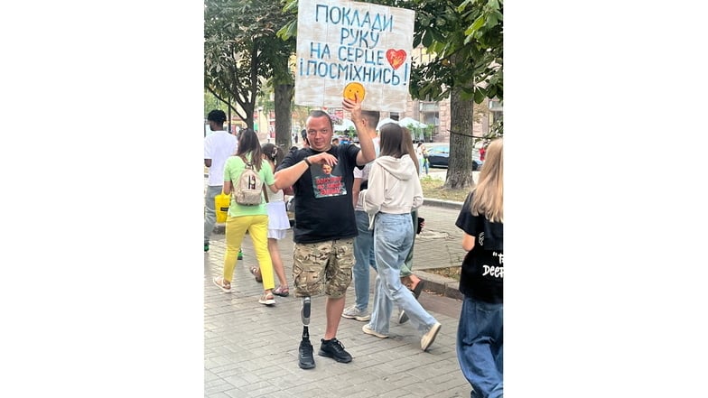 Ein Mann mit Beinprothese hält in der Kiewer Innenstadt ein Plakat mit der Aufschrift: "Lege deine Hand aufs Herz und lächle!"