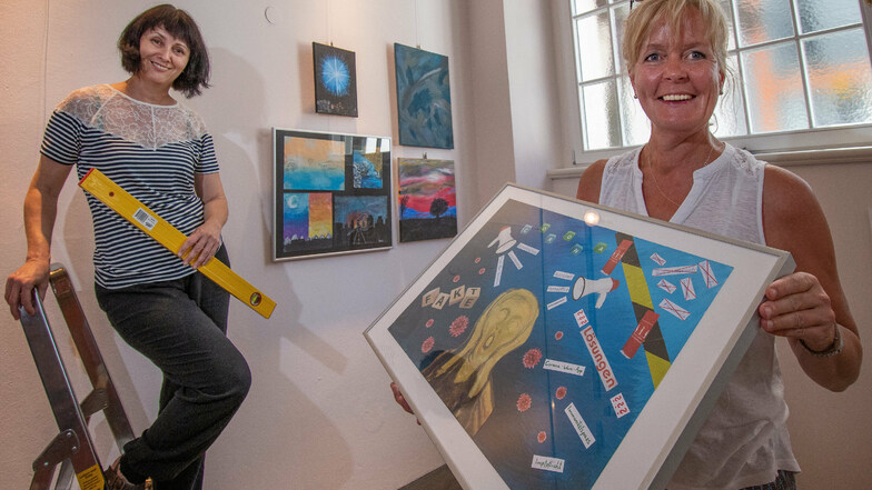 Olga Scheck (links) und Kathrin Fuchs hängen im Treppenhaus des Döbelner Rathauses die Bilder von 17 Hobby-Malern, die sich an dem Projekt „Denkzeit“ beteiligen.
