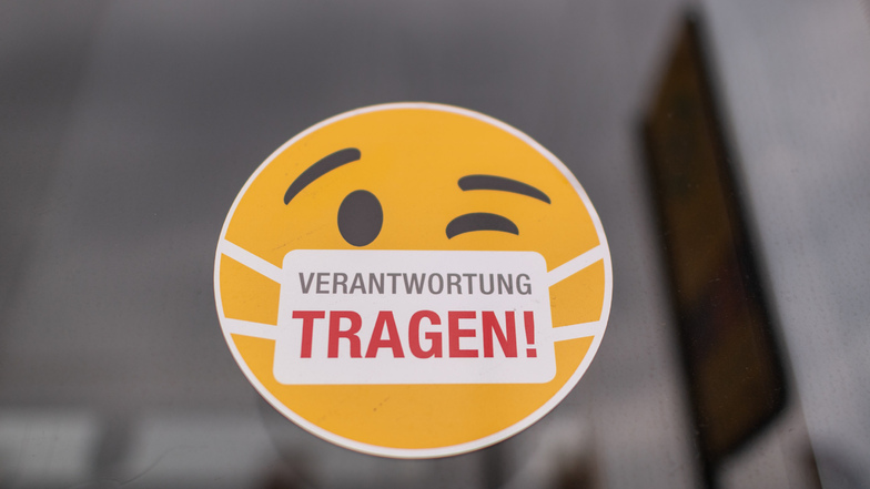 Ein Smiley-Aufkleber mit einem Mundschutz und der Aufschrift "Verantwortung tragen" klebt an der Scheibe einer Dresdner Straßenbahn.