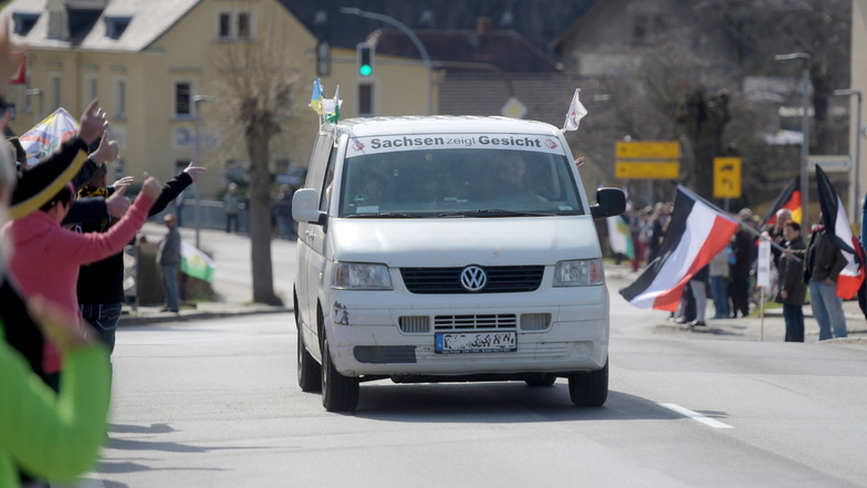 Kritiker der Corona-Maßnahmen grüßen den Fahrer eines VW Busses, der mit der Aufschrift "Sachsen zeigt Gesicht" auf der B96 durch Oppach fährt.