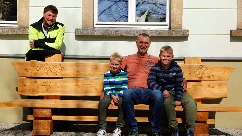 Sie haben schon mal auf der neuen Otto-Garten-Bank in Elstra Platz genommen: Sponsor Uwe König und seine beiden Enkel Levi (l.) und Luca. Im Hintergrund steht Holzkünstler Uwe Hohlefeld, der die Bank geschaffen hat.