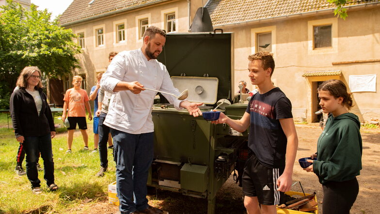 Sebastian Fischer bekochte die Konfirmanden im Camp auf dem Pfarrhof Skassa mit der Gulaschkanone. Auch Elia und Silvie lassen sich die Kartoffelsuppe schmecken.