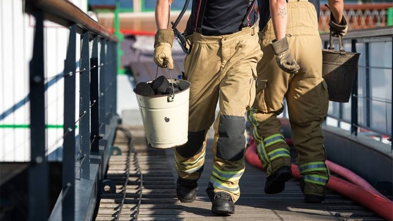 Feuerwehrmänner tragen die Kohlen in Eimern nach draußen.
