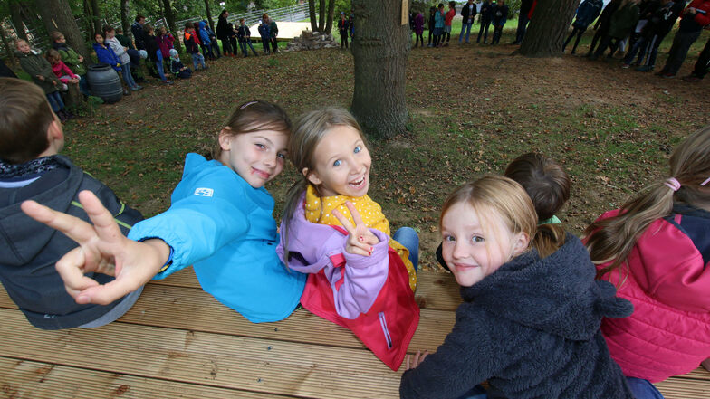 Evely, Maria und Helene sitzen mit ihren Mitschülern auf einem der drei Holzdecks, die im Mußepark an der evangelischen Grundschule entstanden sind.